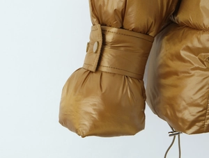 Detail of glossy metallic brown puffer jacket sleeve with elastic cuff and button accents