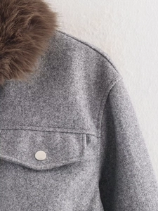 Detail of grey wool jacket featuring brown faux fur collar and silver metal button