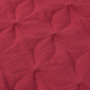 Macro detail of wine red quilted fabric with a precise leaf pattern and fine stitching
