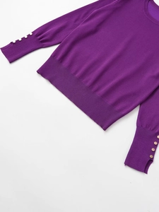 Detail of purple knit sweater showing golden decorative buttons and ribbed texture on sleeve