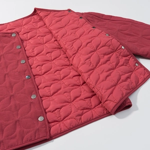 Detail of red quilted jacket showing floral stitching and metal snap button closure
