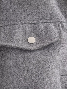 Detail of grey faux fur jacket showing pocket flap and silver metal snap button closure