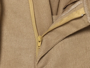 Macro detail of khaki twill trousers showing the precise zipper fly and fabric texture