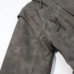 Détail de veste en daim gris foncé avec œillets métalliques et sangles croisées en gros plan
