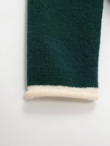 Detail of dark green knit sweater featuring contrast cream roll-edge cuffs and fuzzy texture