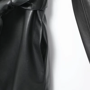 Detail of black faux leather coat featuring a tied waist belt and invisible side pocket