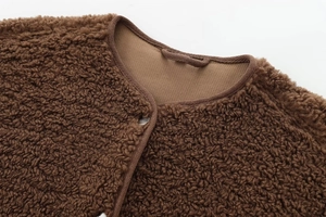 Gros plan sur la texture pelucheuse marron et le col avec détail de bouton en métal