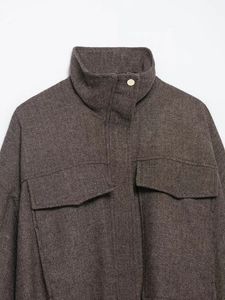 Detail of brown herringbone bomber jacket featuring stand collar and gold metal button