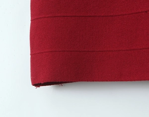 Macro detail of dark red knit fabric showing ribbed texture and rolled hem finish