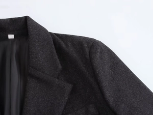 Detailed close-up of dark grey wool suit blazer featuring padded shoulders and notched lapels