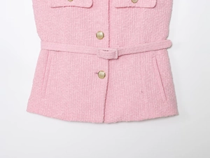 Detail of pink tweed texture and gold buttons on a sleeveless jacket with waist belt