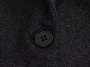 Close-up of the black four-hole button and textured wool fabric on a dark blazer
