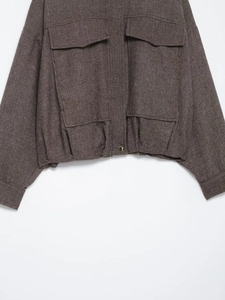 Detail of herringbone bomber jacket featuring large flap pockets and a gold metal button