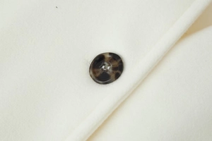 Detail shot of ivory wool coat fabric with a brown tortoiseshell button texture