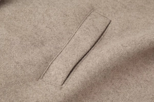 Macro shot of oatmeal wool coat fabric texture and flat welt pocket stitching detail