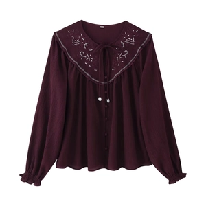 Detail of burgundy long sleeve shirt featuring white radial embroidery and beaded collar