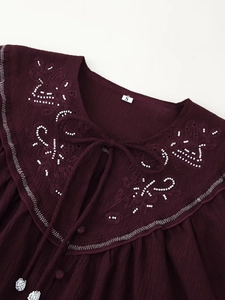 Close-up of wine red blouse with white bead embroidery and delicate doll collar detail