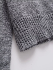 Detailed close-up of grey knit sweater showing fine wool texture and ribbed cuffs