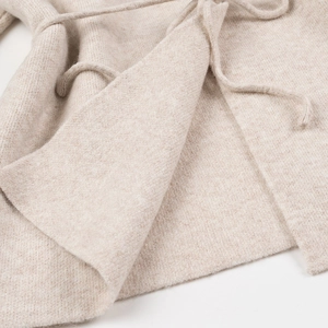 Détail macro de la texture tricotée beige doux et du lien à la taille du cardigan