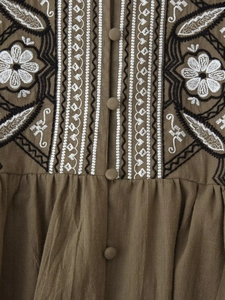 Close-up of bohemian embroidery and fabric-covered buttons on olive cotton-linen shirt