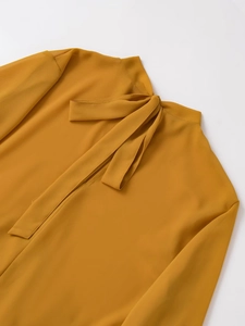 Close-up of mustard yellow long sleeve top featuring an elegant bow tie high neckline