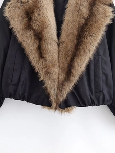 Detail view of stylish jacket featuring a large brown faux fur collar and black matte fabric