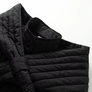 Detail of black quilted stand collar jacket showing snap button and ribbed fabric texture