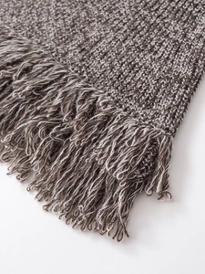 Gros plan sur la maille chinée grise et les longues franges de ce haut tricoté