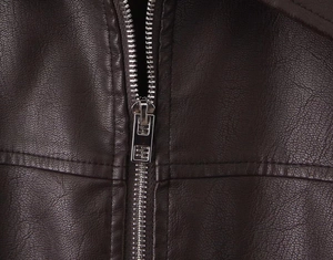 Detailed macro view of dark brown leather jacket featuring silver metal zipper and texture