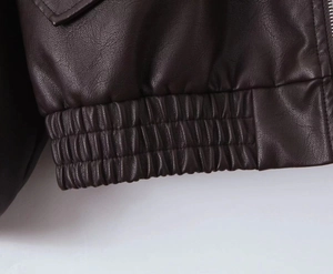 Detail showing elastic hem and grainy texture on brown faux leather jacket with metal zipper