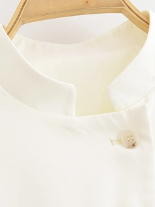 Détail du col montant et du bouton marbré sur une veste courte crème pour femme