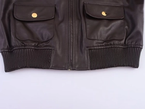 Dettaglio giacca in pelle marrone scuro con fibbie in metallo oro e bordo fondo a coste