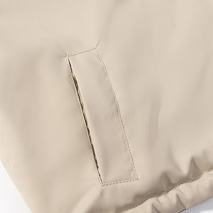 Close-up of side pocket stitching and windproof fabric on a beige hooded cotton jacket
