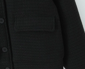 Detailed close-up of black tweed fabric texture and button on women's jacket