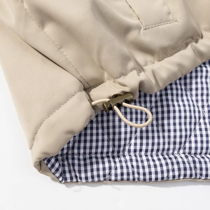 Detail of khaki jacket hem with blue checkered lining and bronze metal drawstring toggle