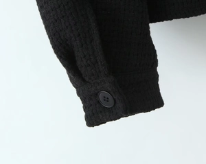 Close-up detail of the black tweed jacket cuff featuring a matte button and woven texture