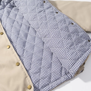 Close-up of diamond quilted beige jacket featuring blue gingham lining and metal snap buttons