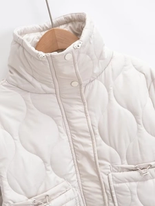 Detail of cream wavy quilted jacket showing stand collar, snap buttons and drawstring hem