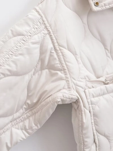 Detail view of wave quilting pattern and metal snap button on creamy white jacket