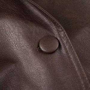 Detail of a brown leather jacket featuring a matching covered button and double stitching