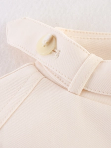 Dettaglio del bottone crema e del passante per cintura su giacca in twill da donna