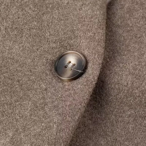 Detail of wool blend coat fabric with amber textured button and fine stitching