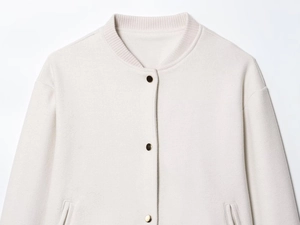Close-up of cream baseball jacket with golden snap buttons and ribbed knit collar detail