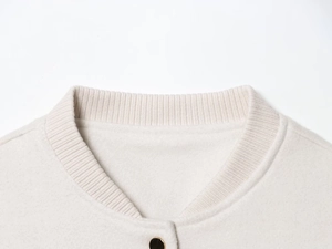 Detail of ribbed knit collar and golden metal button on beige varsity jacket