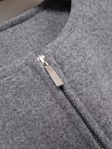 Detail view of grey tweed jacket showing textured fabric and silver metal zipper closure