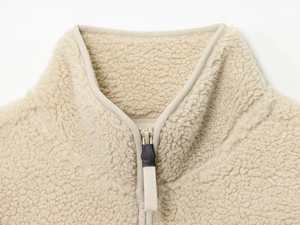 Détail de la texture polaire sherpa beige avec fermeture éclair et tirette en caoutchouc