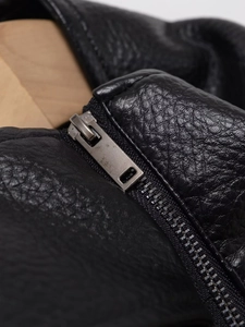 Détail d'une veste en similicuir noir à grain litchi avec fermeture éclair en métal vieilli