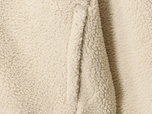 Détail rapproché de la texture du tissu polaire Sherpa beige avec coutures de qualité