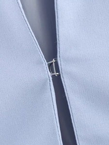 Vista macro di un blazer azzurro con chiusura a gancio in metallo e trama del tessuto