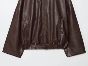Détail d'une veste en cuir marron foncé avec poches à fermeture éclair et boucle de ceinture